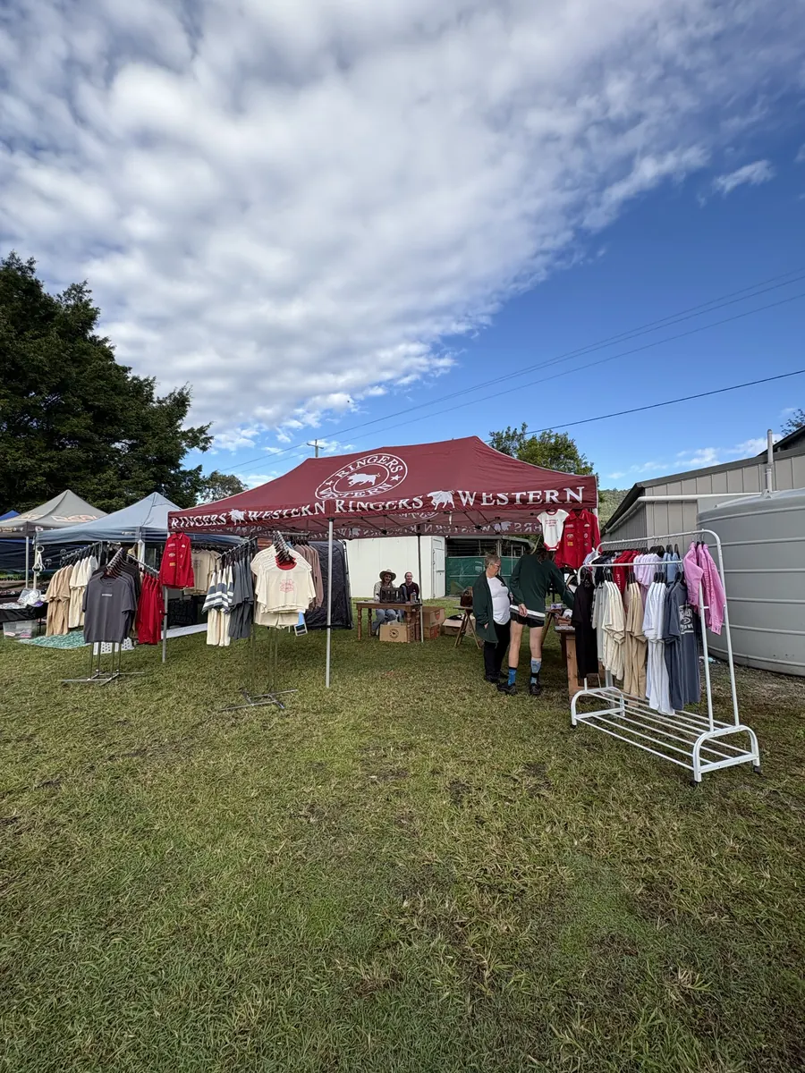 A wide view along the market row, marquees and clothing racks on open grass