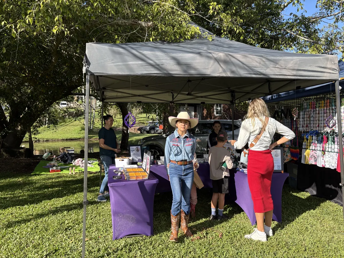 A stallholder in a western shirt serving customers at a marquee stall on the grass