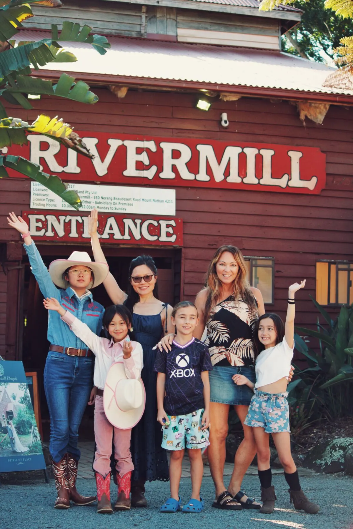 Two mums and four happy kids cheering under the Rivermill entrance sign