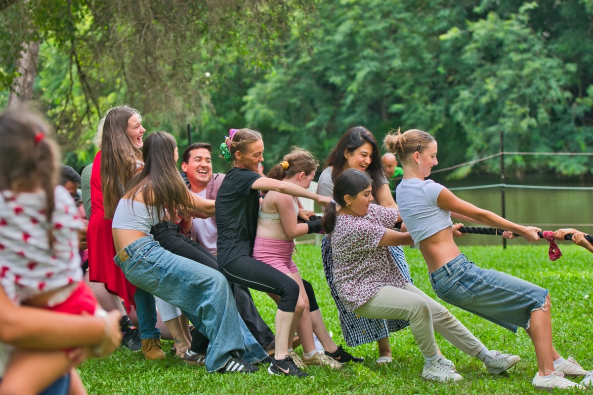 A laughing group leaning back on the rope in a tug of war on the riverside lawn at Historic Rivermill
