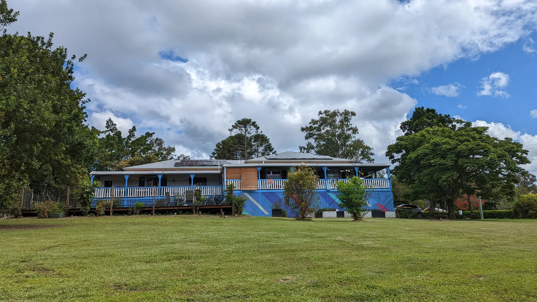 The farm-stay house at Historic Rivermill, a high-set timber house with a wraparound verandah, seen across its lawn under a big sky