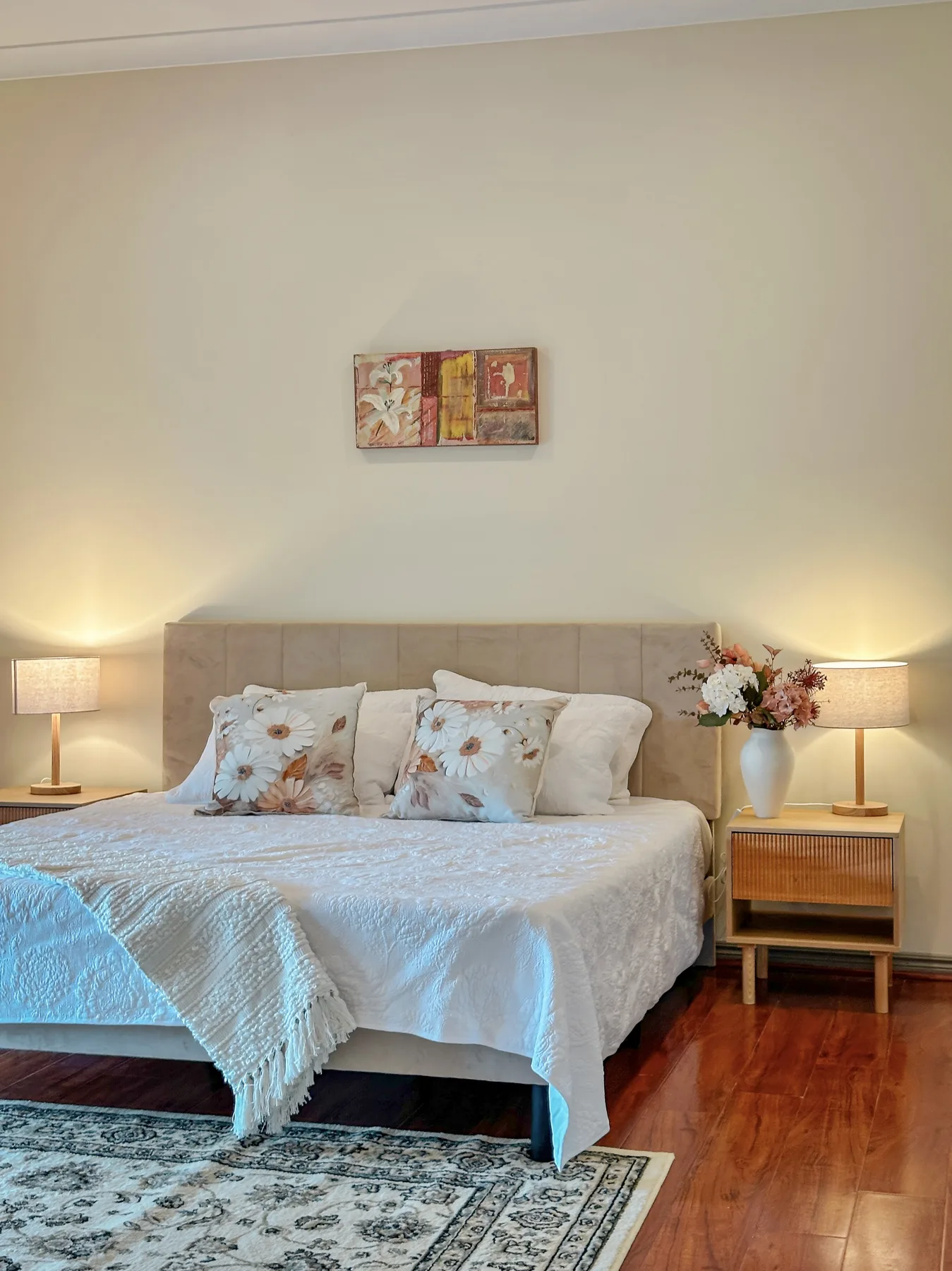 The king bedroom, with bedside lamps lit, fresh flowers and a patterned rug on polished floorboards