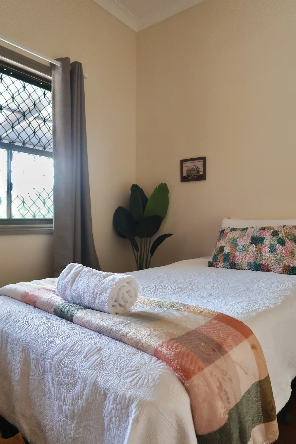 A bedroom with a plaid throw, rolled towels and a window onto the trees