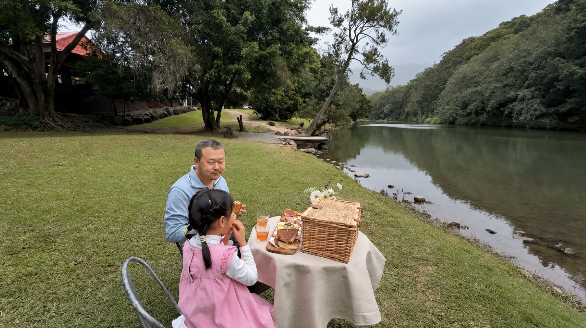 A dad and his daughter sharing a picnic hamper on the grassy bank of the Coomera River at Historic Rivermill