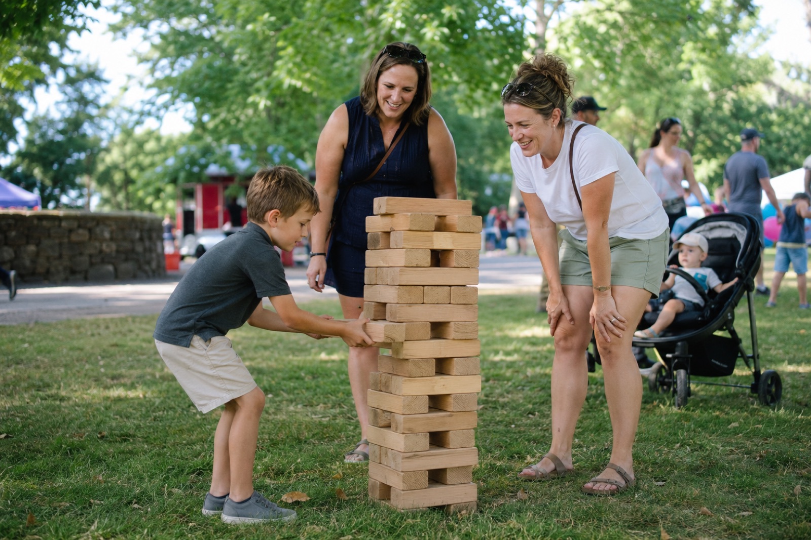 A child and two mums playing giant Jenga on the grass at Historic Rivermill