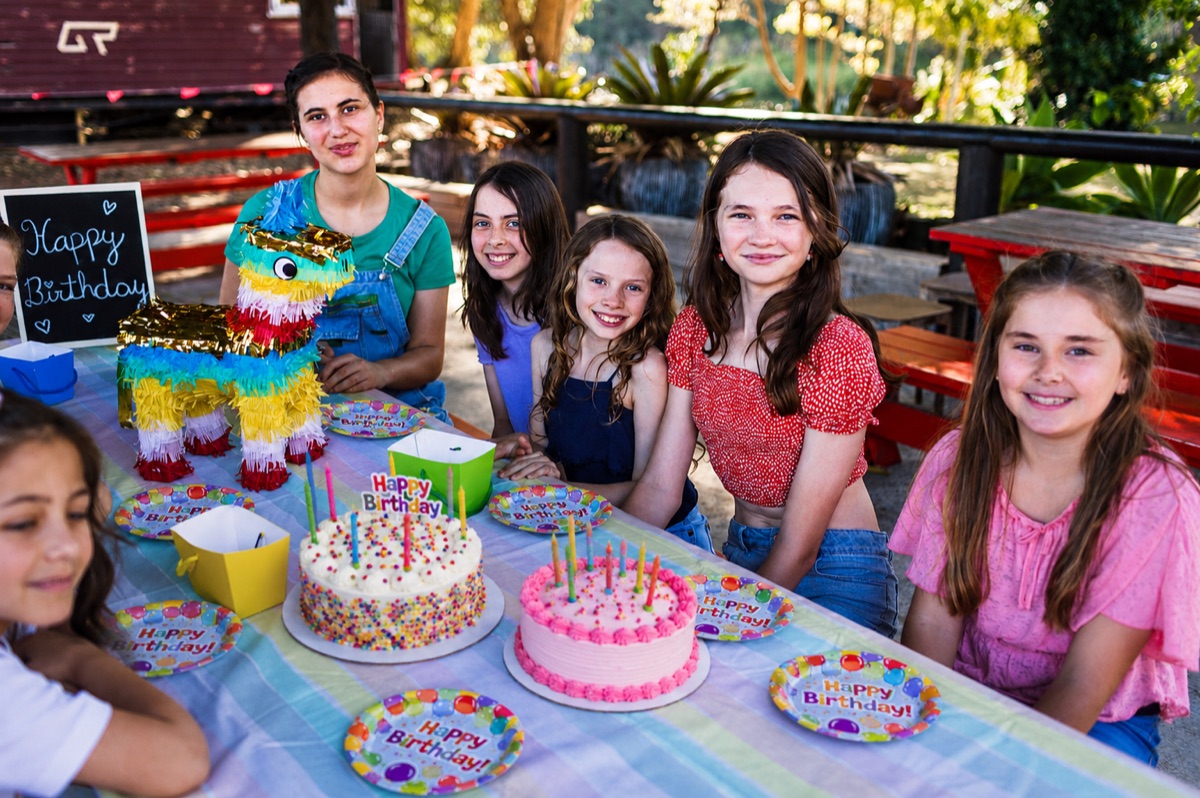 Children around a birthday table with two iced cakes, party plates and a piñata at Historic Rivermill