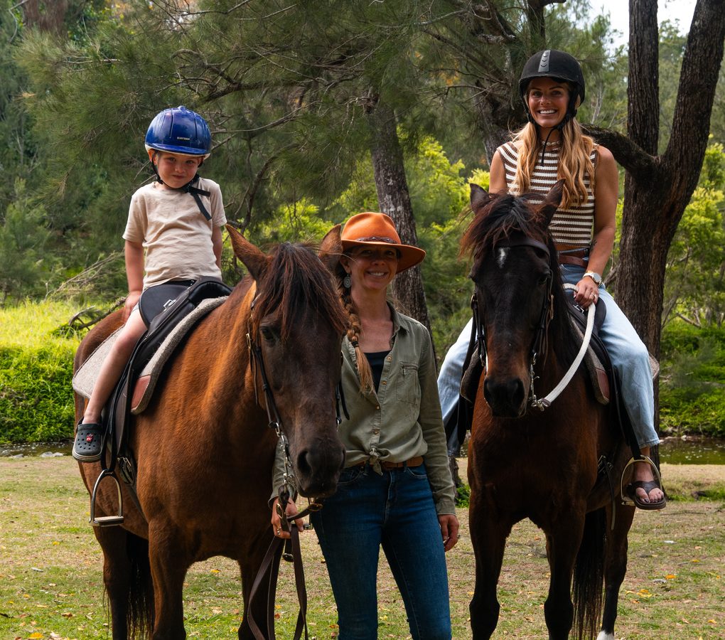 A young rider and an adult rider each on their own horse, with their guide standing between them