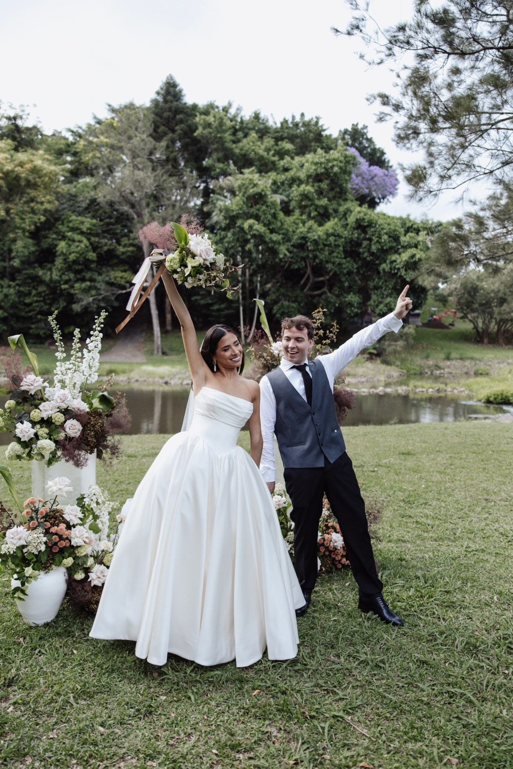 The newlyweds cheering, bouquet raised, on the ceremony lawn