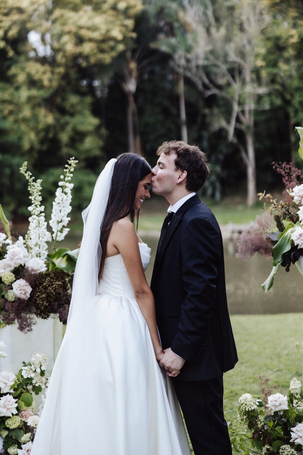 The groom kissing the bride's forehead among the ceremony florals